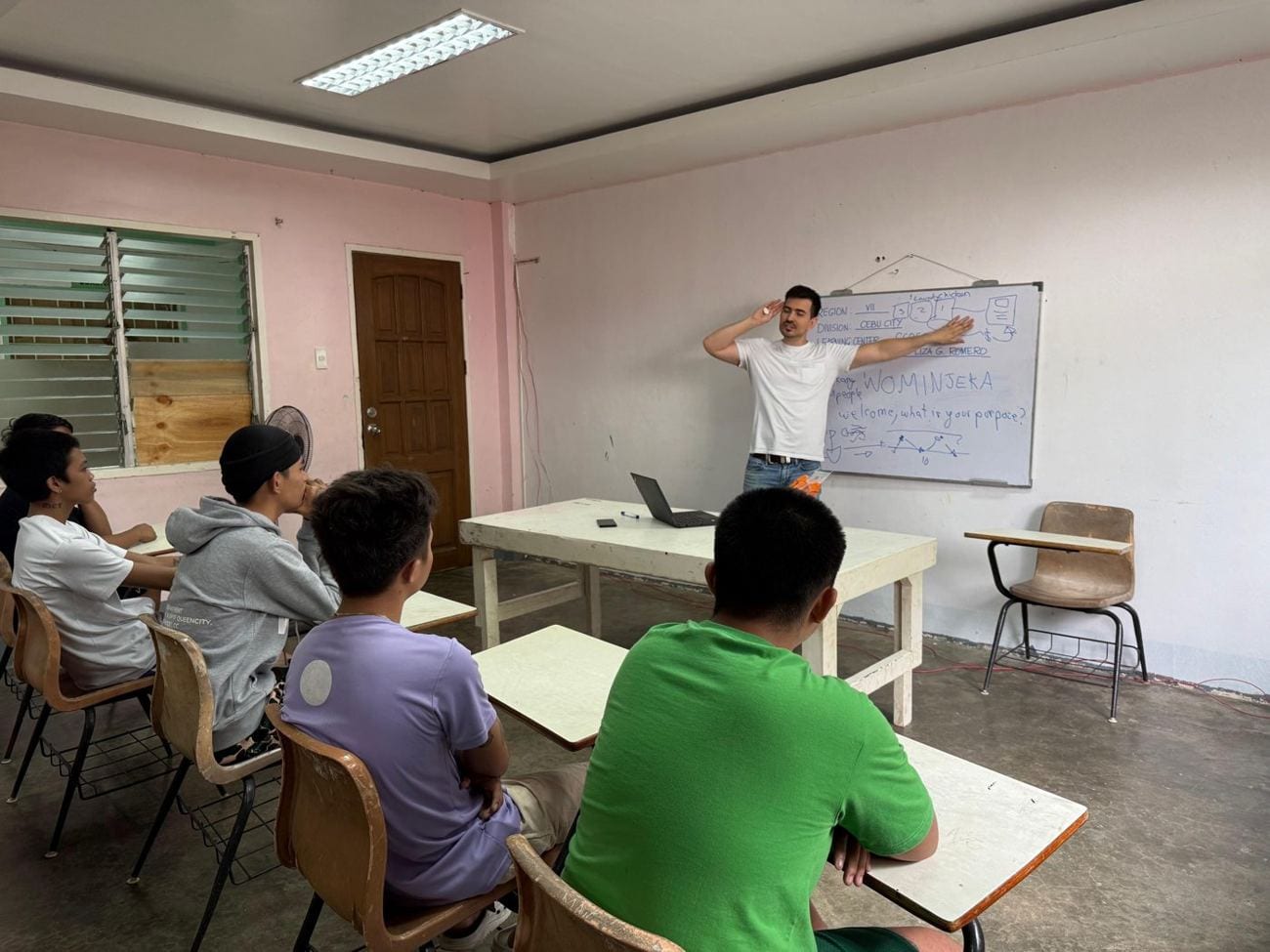 A session in Cebu City: students at desks facing a whiteboard that reads Wominjeka — welcome, what is your purpose?